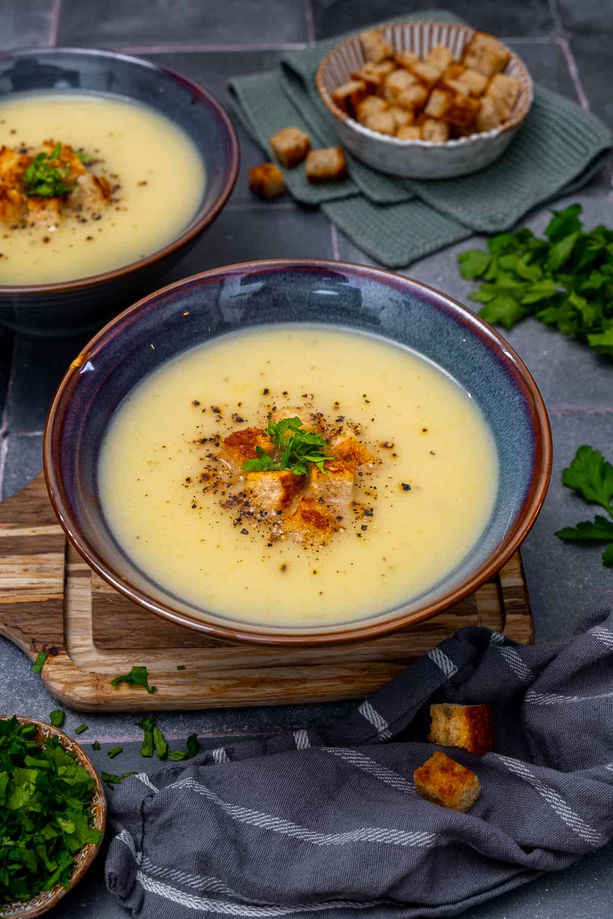 Jerusalem artichoke soup topped with croutons, parsley and pepper in a bluish bowl.