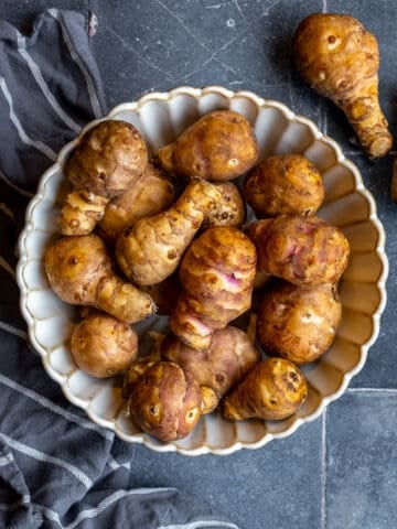Jerusalem artichokes photographed in a white bowl and on dark grey tiles.