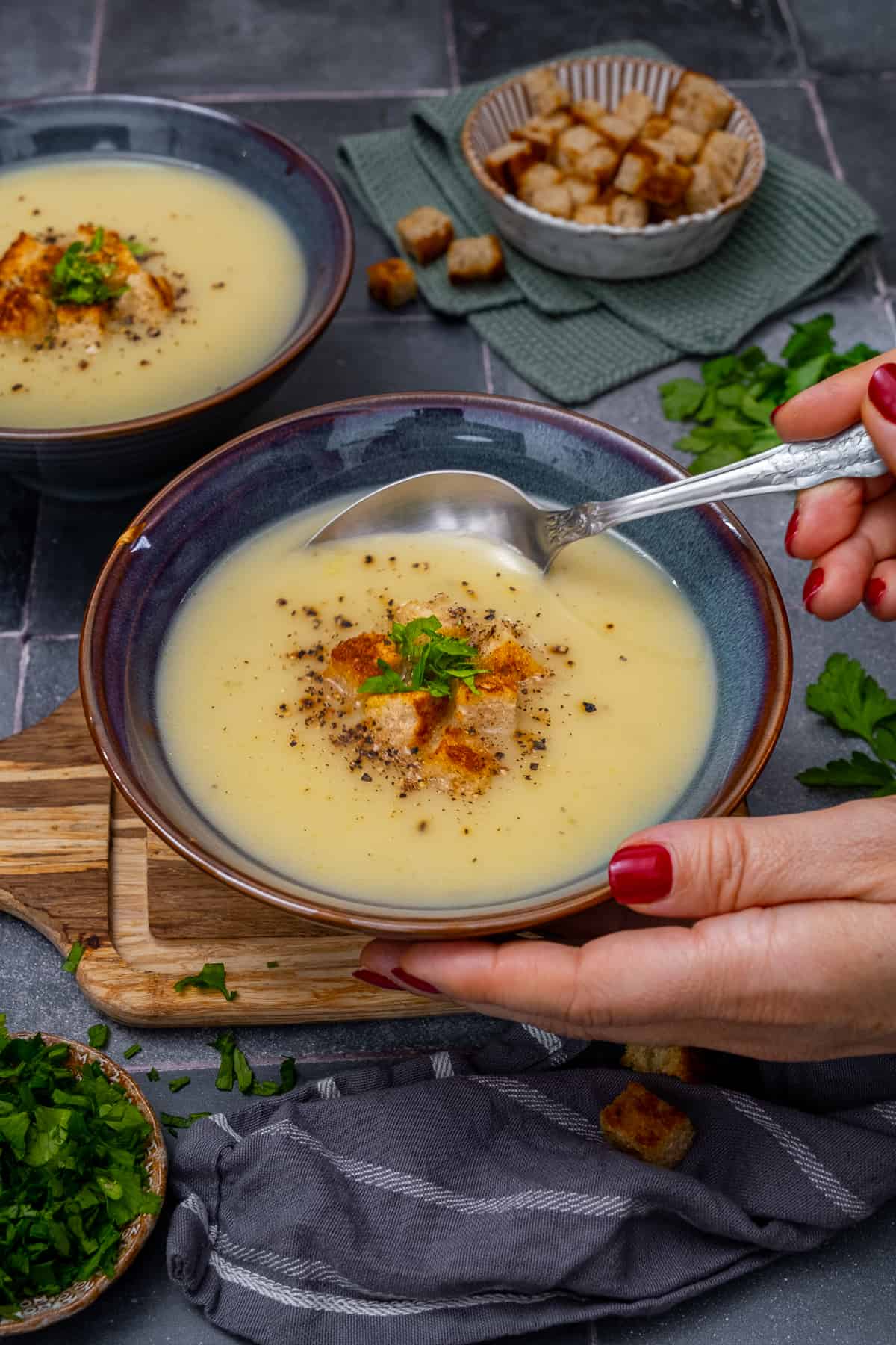 Hands holding a bowl of Jerusalem artichoke soup and placing a spoon inside it.