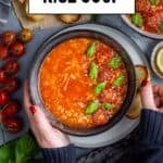 Hands holding a bowl of tomato rice soup garnished with cherry tomatoes and fresh basil, with bread slices and ingredients around, and text "Tomato Rice Soup" and "giverecipe.com".