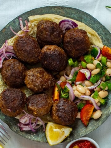 Meatballs and bean salad with onions and tomatoes served on some bread on a copper plate.