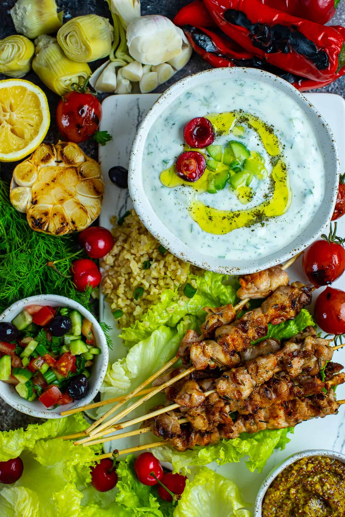 Turkish cacik in a bowl served on a platter of chicken shish kebabs and more side dishes.
