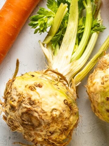 Image of a whole celeriac with its greens and a carrot on the side.
