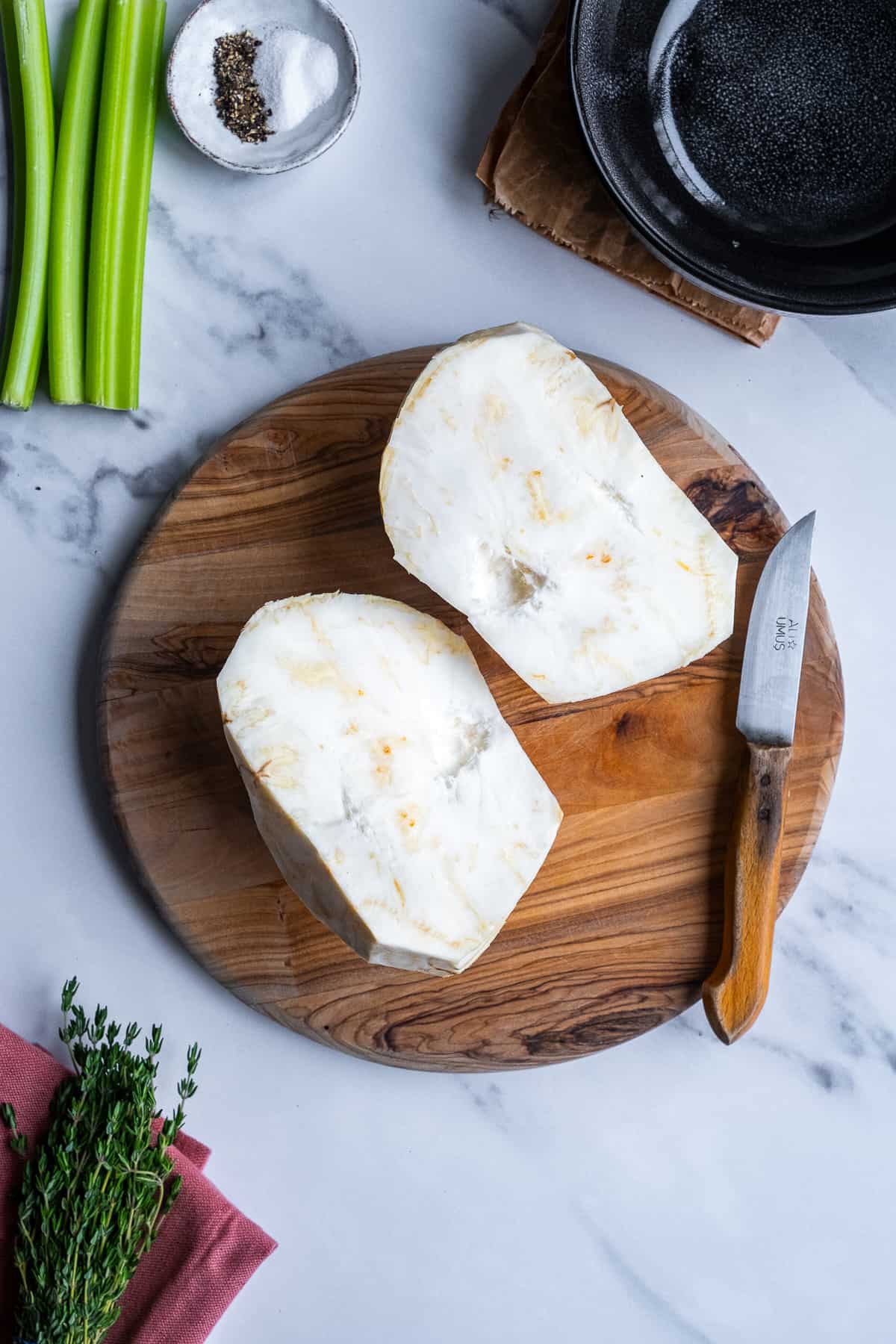 A celeriac peeled and halved on a wooden cutting board, a knife on the side.