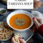 Woman hands holding a bowl of soup and some piece of flatbread accompanied by spices and Turkish tarhana in a jar.