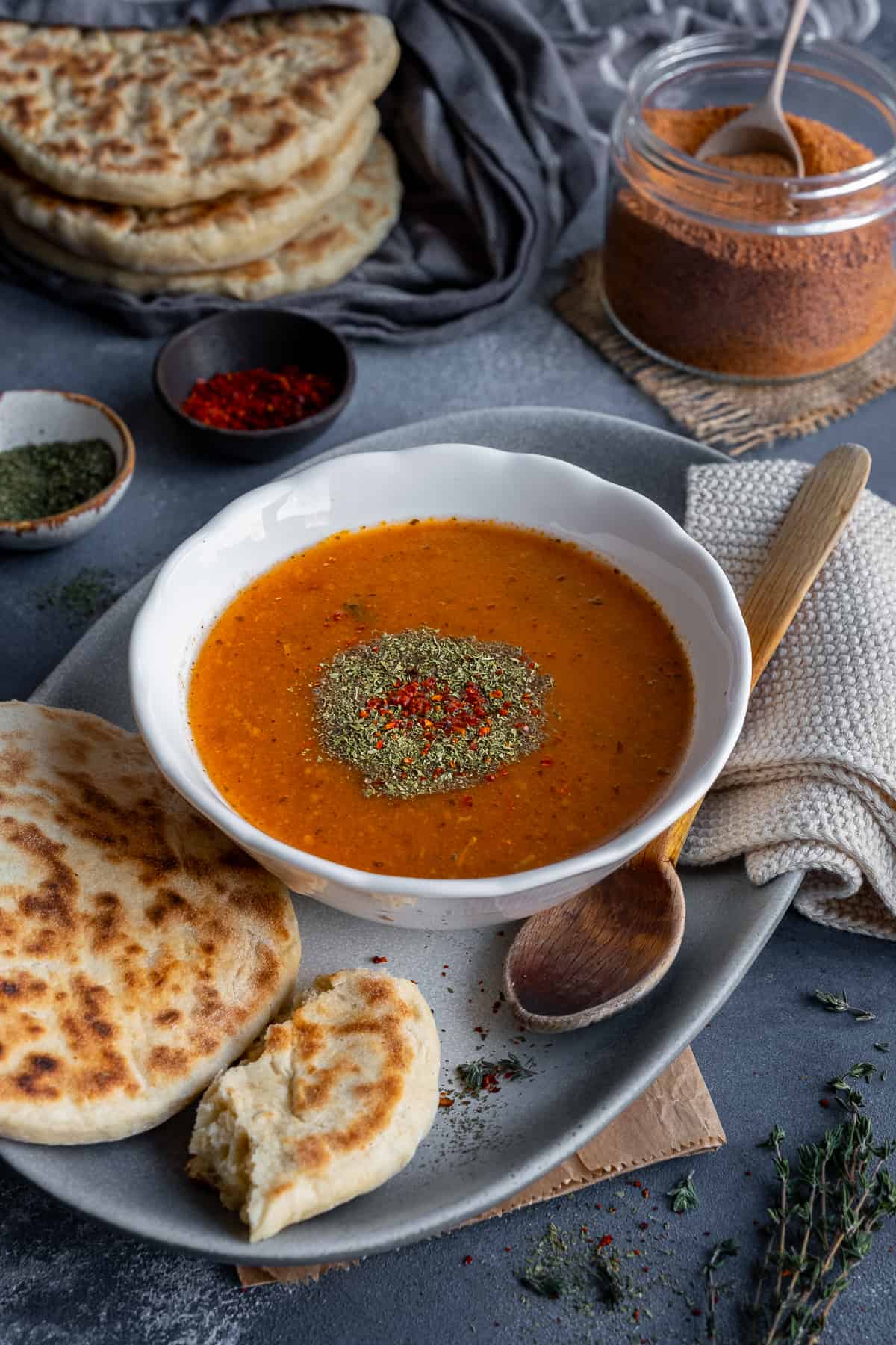 A bowl of tarhana soup garnished with dried mint and red pepper flakes, some bread and a wooden spoon on the side.