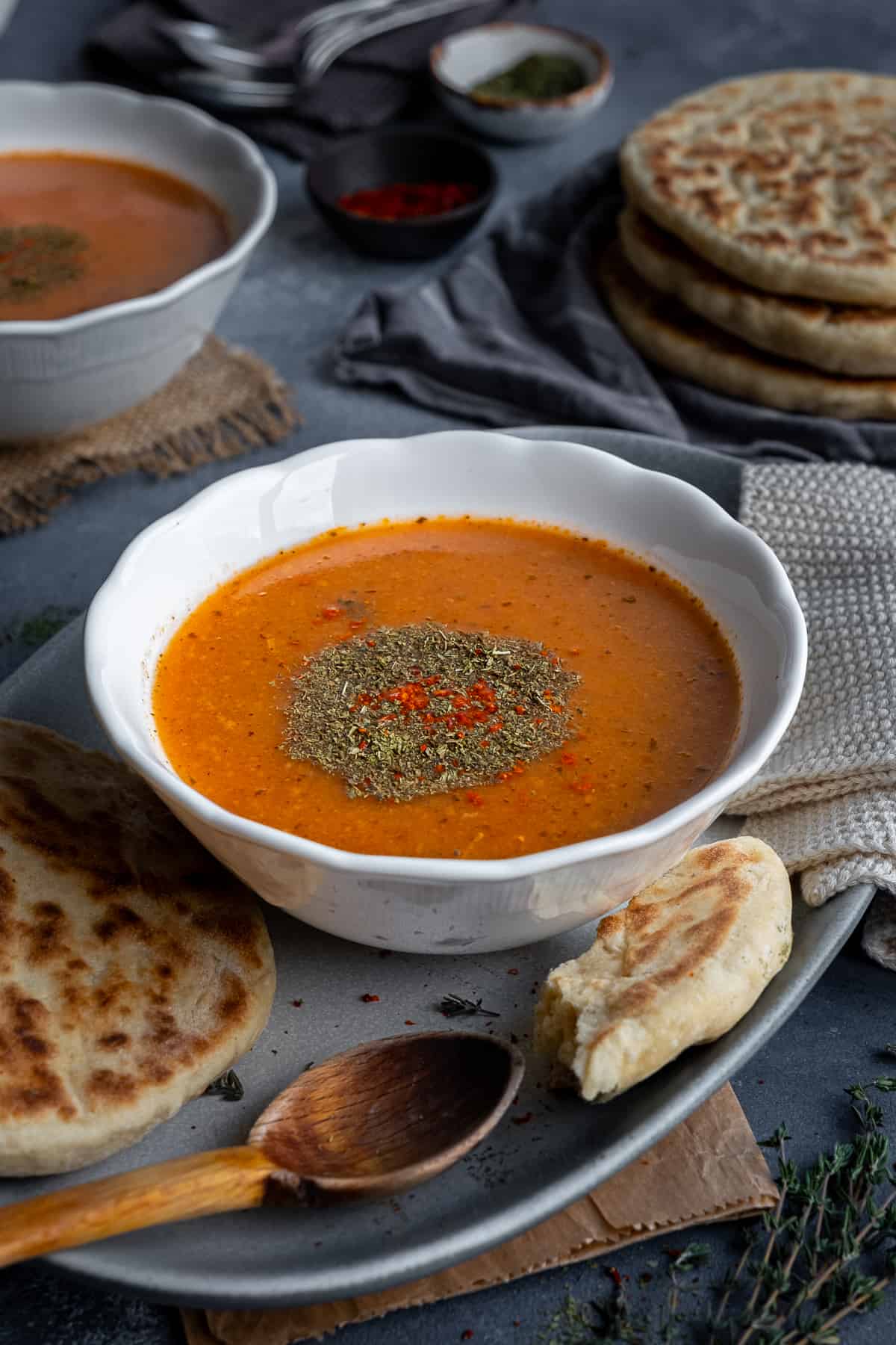 A bowl of tarhana soup garnished with dried mint and red pepper flakes, some bread and a wooden spoon on the side.