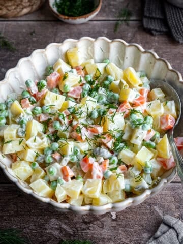 Russian salad in a white bowl and a spoon inside it.