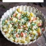 Russian salad in a white bowl and a spoon inside it photographed from front view.