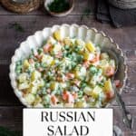 Russian salad in a white bowl and a spoon inside it photographed from front view.