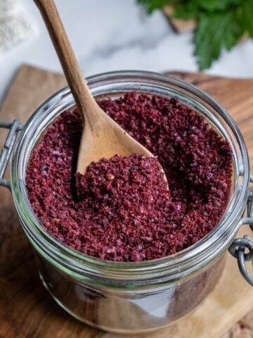 Ground sumac in a glass jar and a wooden spoon inside it.
