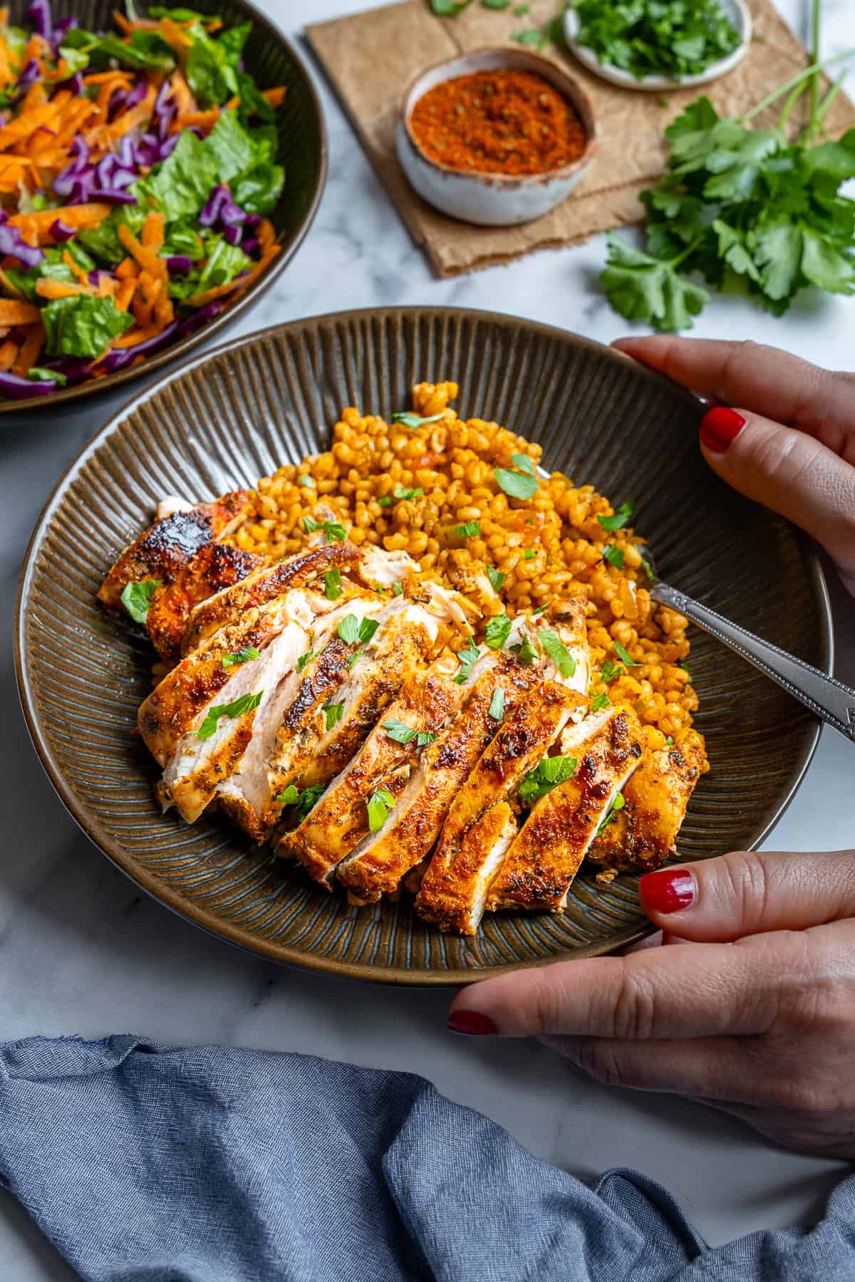 Pan-fried chicken breast sliced and served with bulgur pilaf in a brown bowl and a woman holding it.