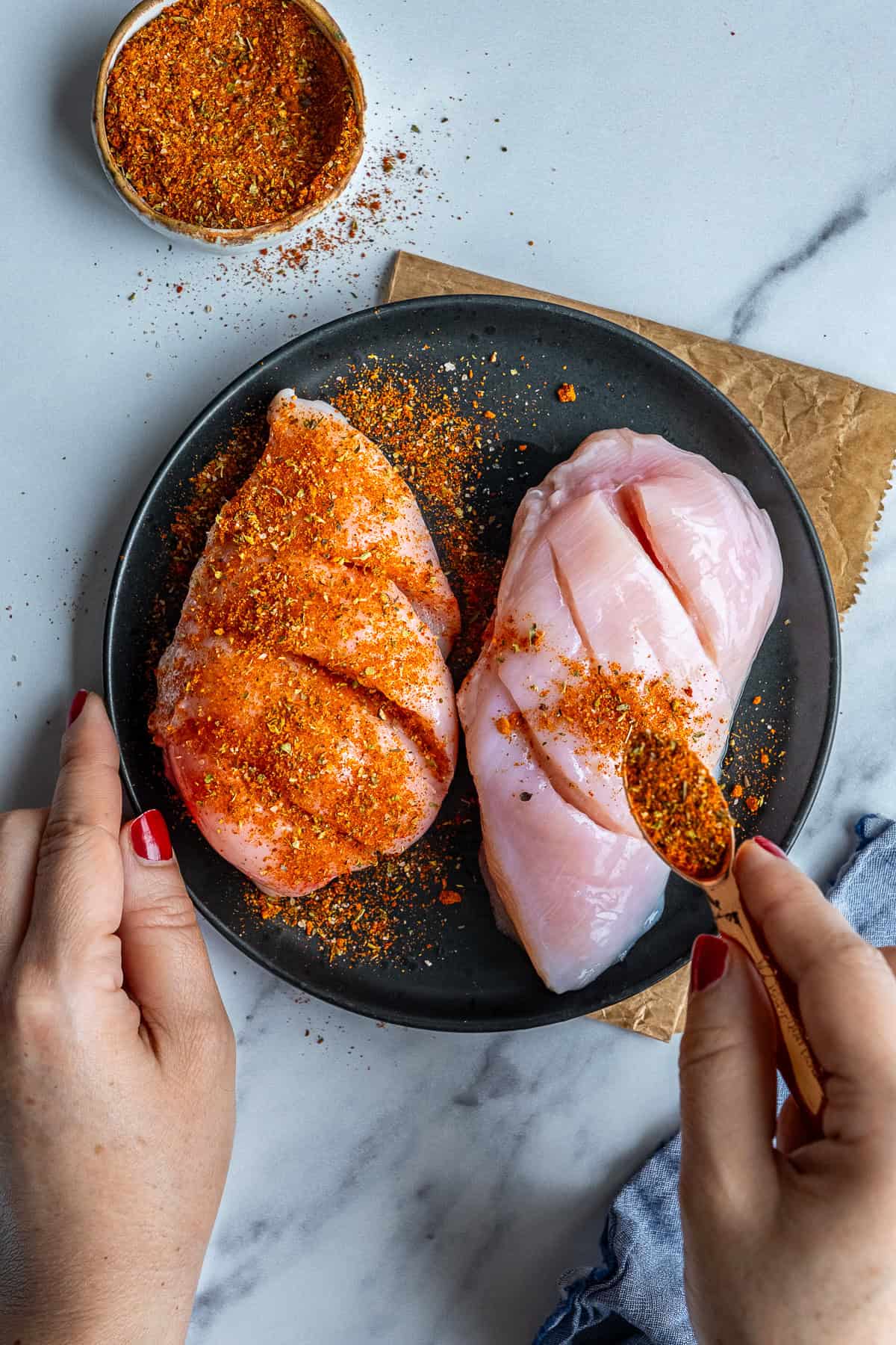 Turkish spice mix being sprinkled over uncooked chicken breasts.