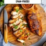 Pan-fried chicken breasts on a round wooden cutting board and a spice mix in a small bowl on the side.