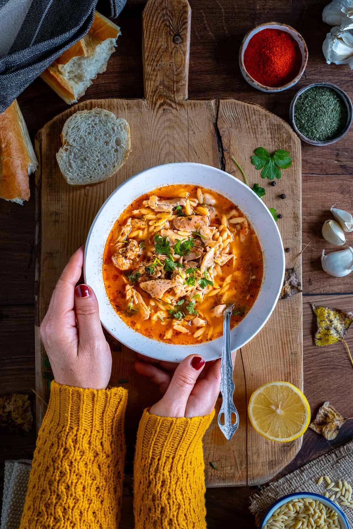 Woman holding a bowl of Turkish chicken soup garnished with parsley.