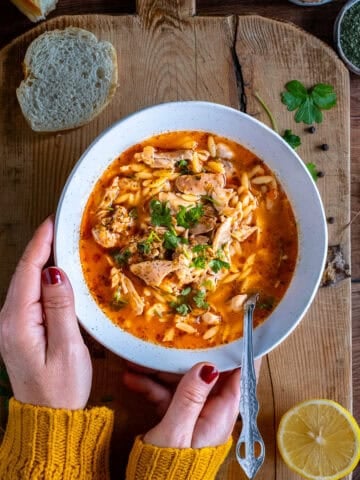 Woman with a yellow jumper holding a bowl of Turkish chicken soup on a wooden board.
