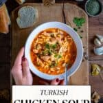 Woman holding a bowl of Turkish chicken soup on a wooden board.
