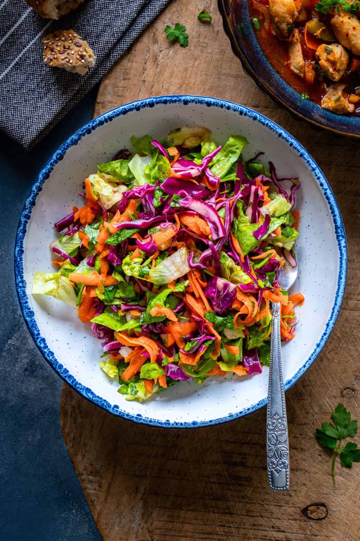 A bowl of lettuce salad with shredded carrot and thinly sliced red cabbage in a white bowl.
