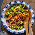 A fresh salad with lettuce, carrots and red cabbage in a white bowl and wooden spoons inside it.
