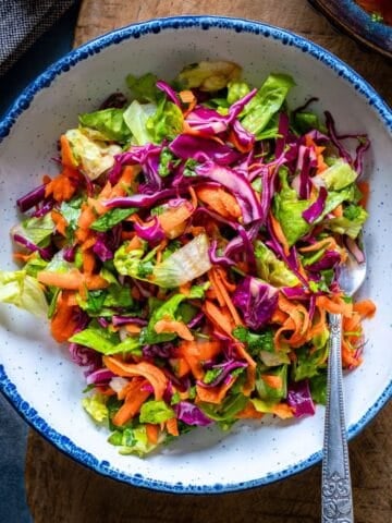 A bowl of lettuce salad with shredded carrot and thinly sliced red cabbage in a white bowl.