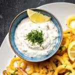 Tarator sauce garnished with chopped parsley and a slice of lemon in a bowl accompanied by fried calamari.