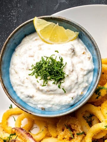 Tarator sauce garnished with chopped parsley and a slice of lemon in a bowl accompanied by fried calamari.