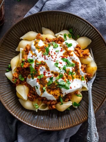 Turkish Pasta with shell pasta, ground beef sauce, garlic yogurt, and spiced butter, garnished with parsley and red pepper flakes in a rustic bowl.