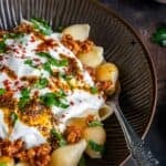 Turkish Pasta with shell pasta, ground beef sauce, garlic yogurt, and spiced butter, garnished with parsley and red pepper flakes on a dark rustic background.