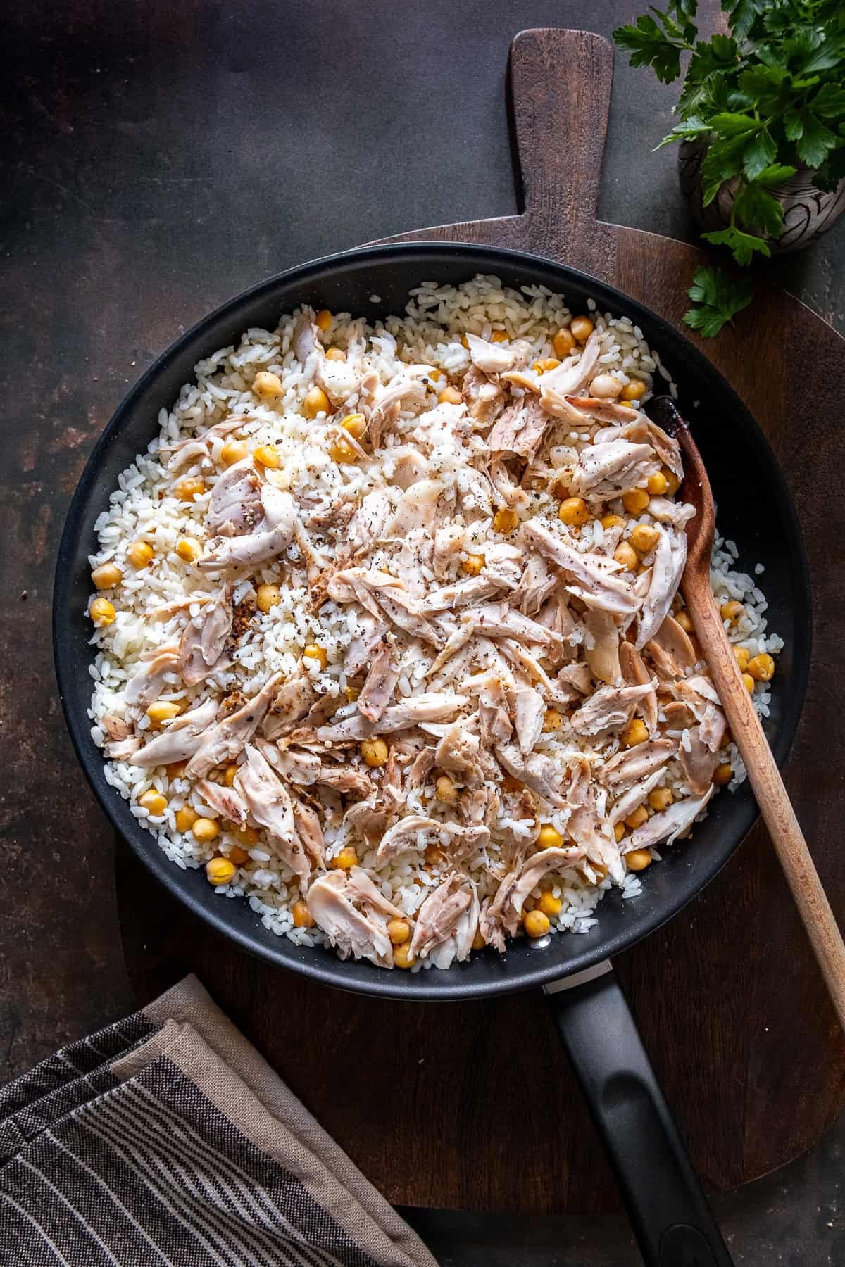 Turkish Tavuklu Pilav in a pan with shredded chicken and chickpeas over rice, topped with black pepper and served with a wooden spoon.