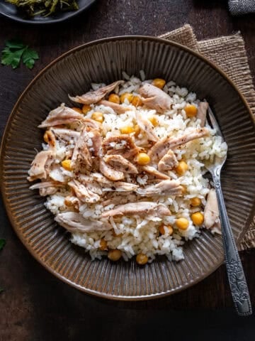A plate of Turkish rice with shredded chicken and chickpeas (Tavuklu Pilav), served with a fork on a rustic table.