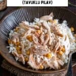 Close-up of a bowl of Tavuklu Pilav (Turkish rice with shredded chicken and chickpeas), served with black pepper on top and pickles in the background.