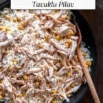 Turkish Tavuklu Pilav in a pan with shredded chicken and chickpeas over rice, topped with black pepper and served with a wooden spoon.