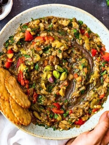 A bowl of chunky baba ganoush without tahini, made with roasted eggplant, tomatoes, herbs, and topped with pistachios, served with crackers.