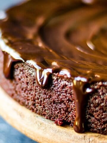 Close-up of a moist chocolate beet cake with glossy chocolate ganache dripping down the sides, served on a wooden board.