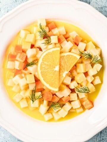 A plate of Turkish-style olive oil braised root vegetables, featuring diced carrots and celeriac in a citrusy sauce, garnished with orange slices and fresh dill.