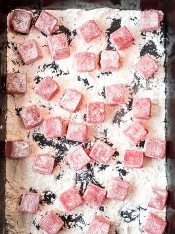 A tray of pink Turkish delight cubes dusted with powdered sugar, scattered over a layer of starch.