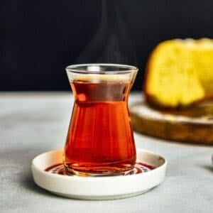 A steaming glass of Turkish black tea served in a traditional tulip-shaped glass on a small saucer.