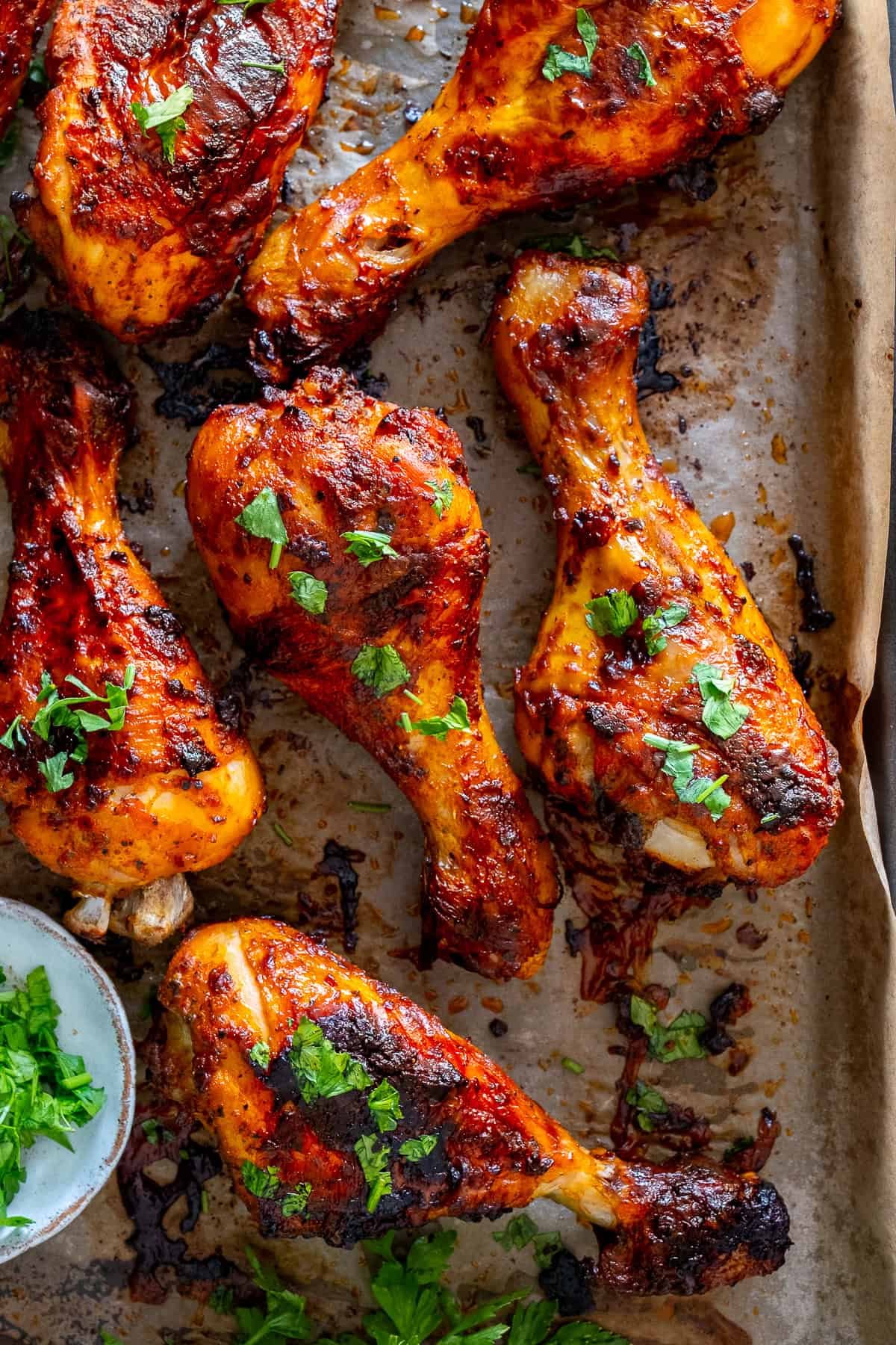 Close-up of oven-baked chicken drumsticks with Turkish marinade, garnished with chopped parsley on a parchment-lined tray.