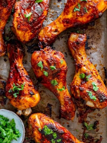 Golden brown chicken drumsticks baked with Turkish marinade, topped with fresh parsley on a parchment-lined baking tray.