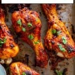 Close-up of oven-baked chicken drumsticks with Turkish marinade, garnished with chopped parsley on a parchment-lined tray.
