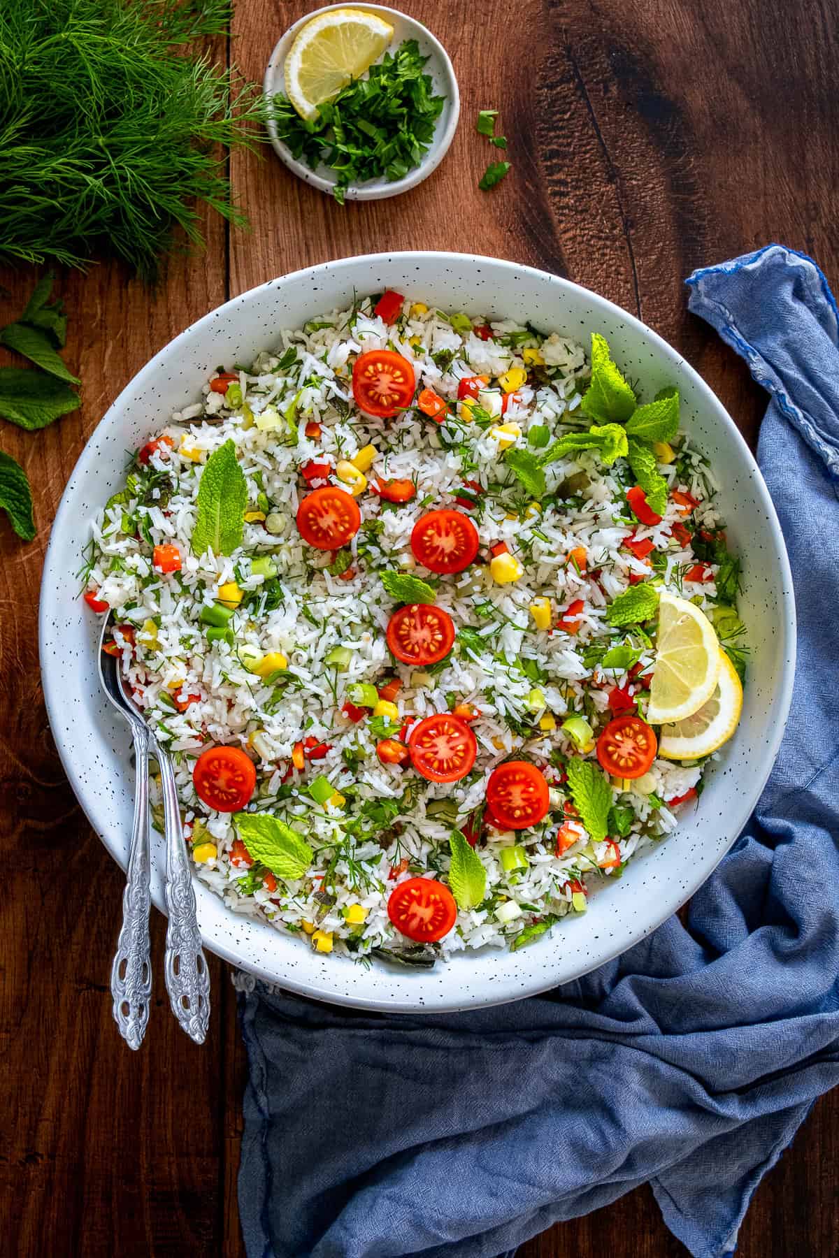 A vibrant Turkish rice salad with cherry tomatoes, herbs, corn, and red peppers, served in a white bowl with lemon slices and fresh mint.