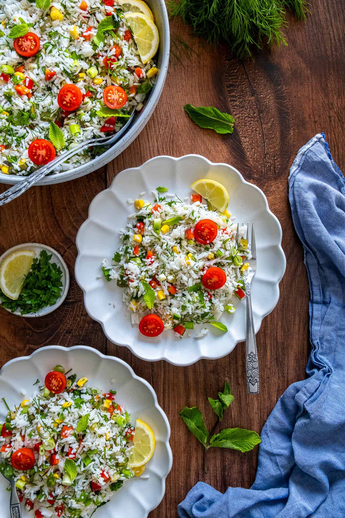 Turkish rice salad served on three white plates with cherry tomatoes, lemon slices, and fresh herbs on a wooden table.