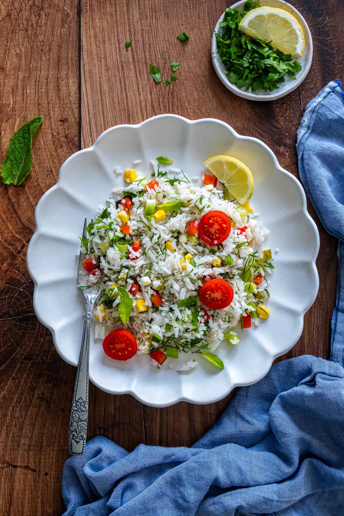 A plate of Turkish rice salad with cherry tomatoes, lemon wedge, and fresh herbs, served with a fork on a wooden table.