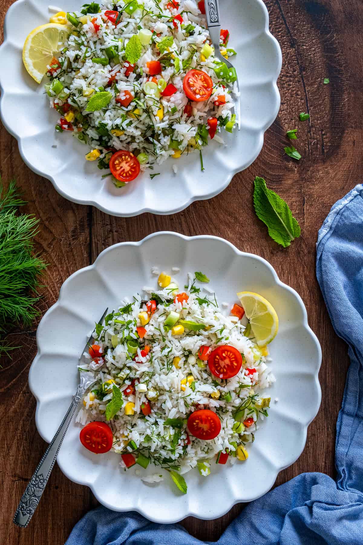 Two plates of Turkish rice salad with cherry tomatoes, lemon slices, and fresh herbs on a wooden surface.