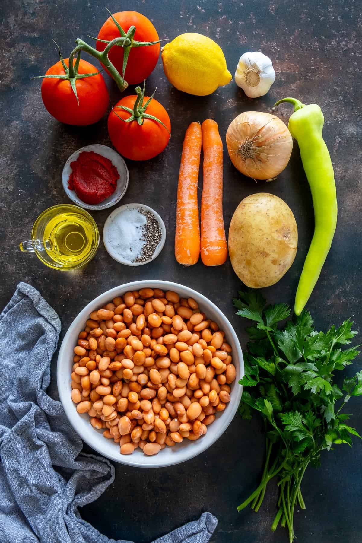 Ingredients for Turkish barbunya pilaki, including borlotti beans, tomatoes, carrots, potato, onion, green pepper, parsley, garlic, lemon, olive oil, and tomato paste.