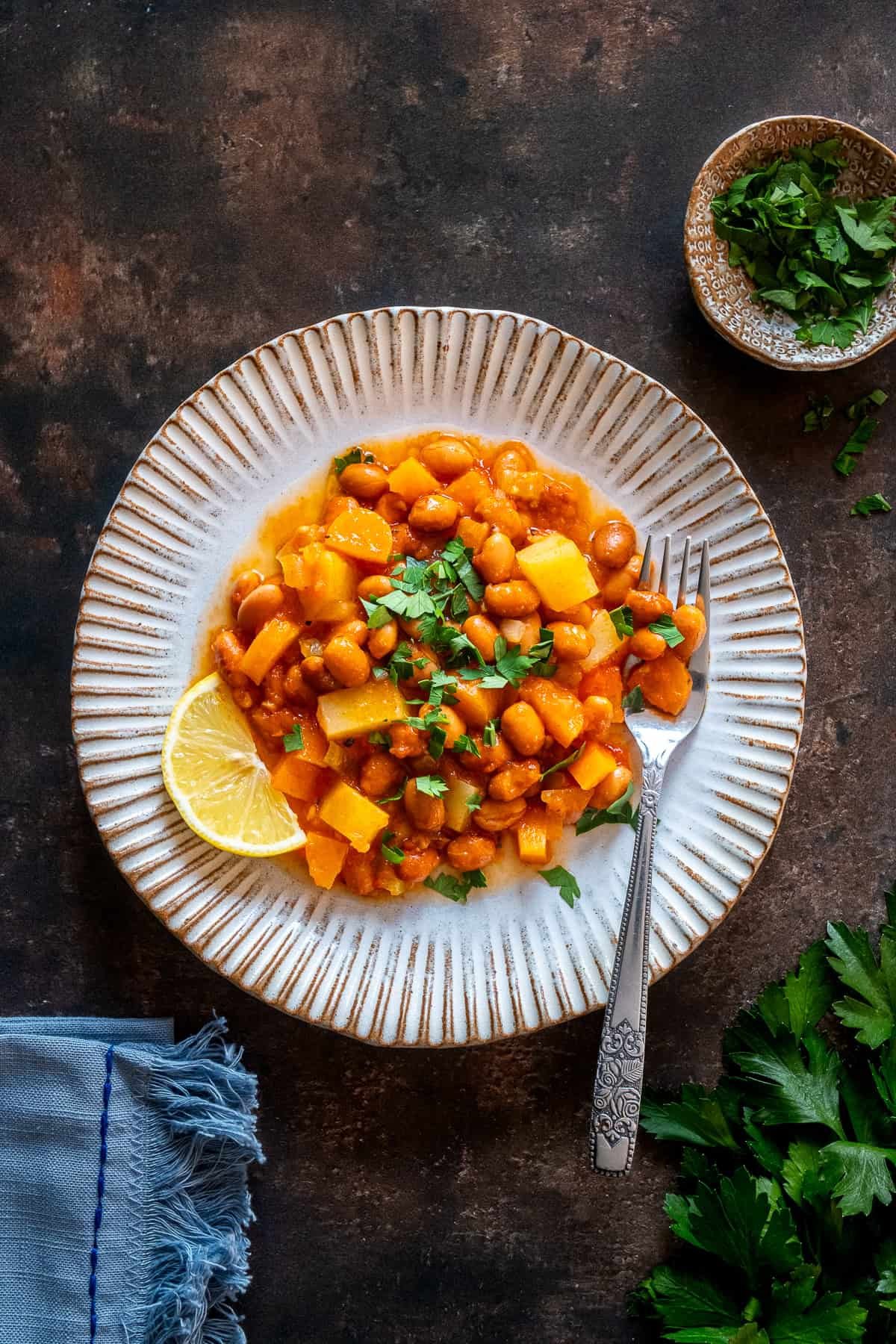 Overhead shot of a plate of Turkish barbunya pilaki with potatoes and carrots, garnished with parsley and a lemon wedge.