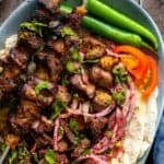 Overhead view of grilled Turkish liver kebabs on skewers served with lavash bread, sumac onion salad, sliced tomatoes, and green peppers.