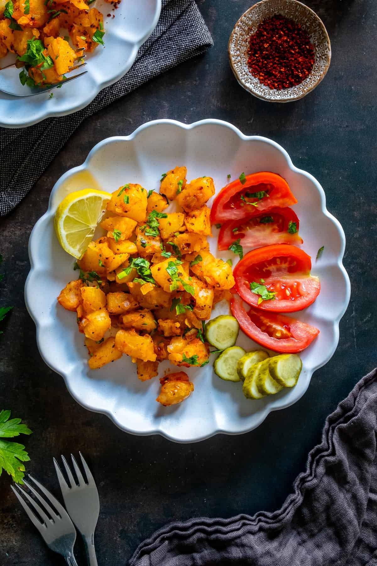 Patates Kavurma served on a white plate with lemon, sliced tomatoes, pickles, and parsley.