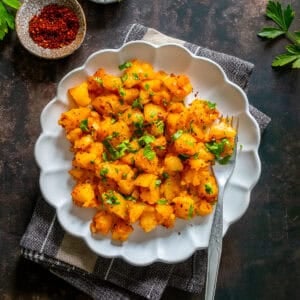 Patates Kavurma, a Turkish potato dish with onion, tomato paste, and spices, served on a white plate and topped with parsley.