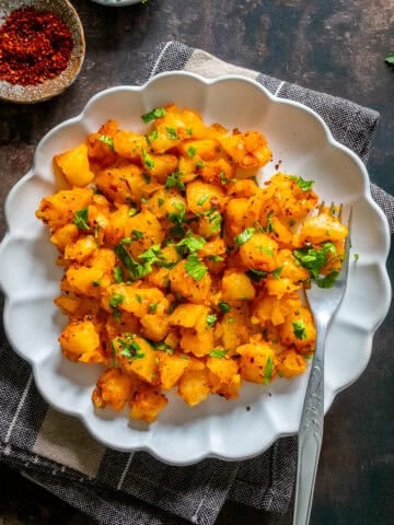 Patates Kavurma, a Turkish potato dish with onion, tomato paste, and spices, served on a white plate and topped with parsley.